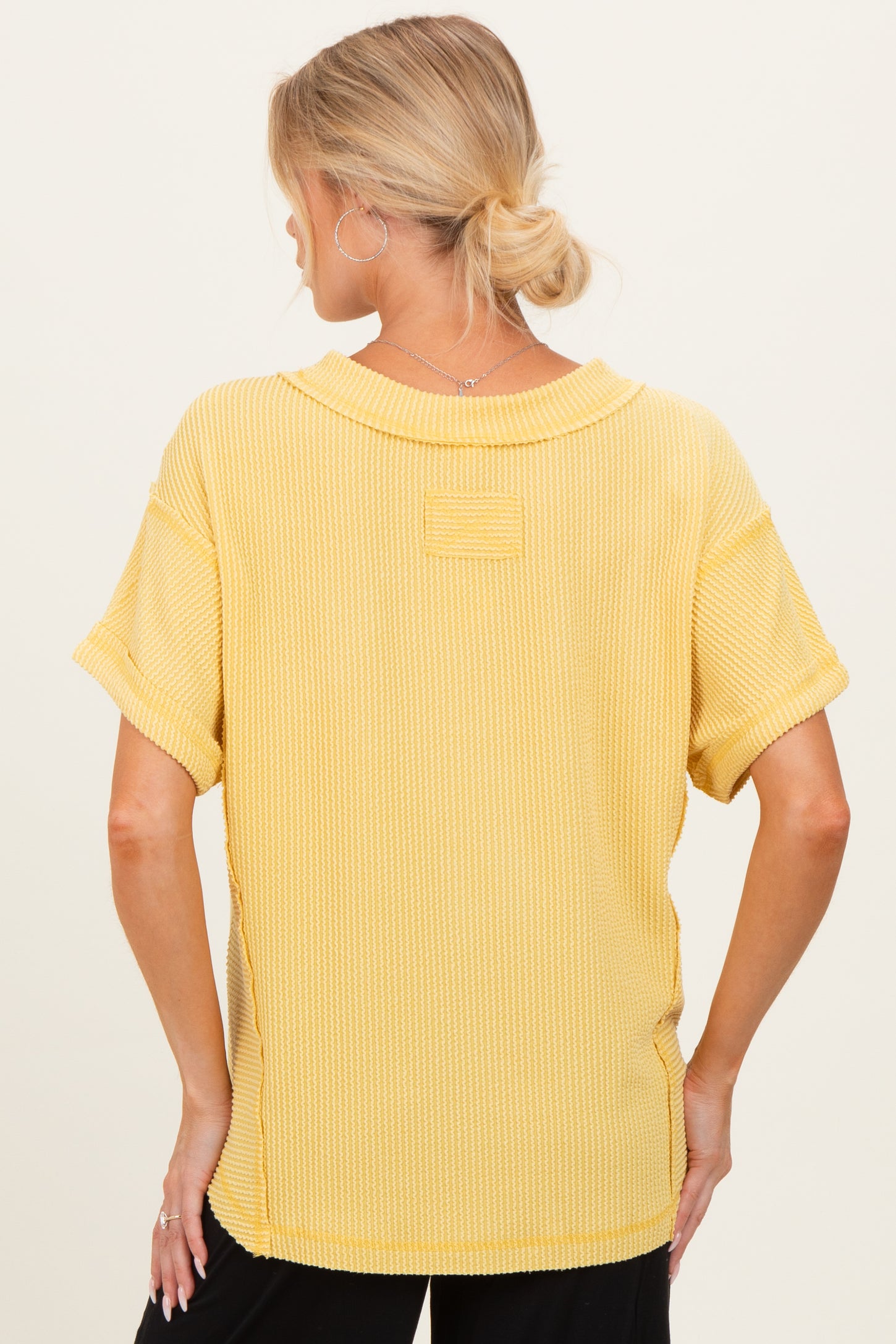 woman wearing a yellow short sleeve maternity top with a relaxed fit and textured fabric, seen from the back
