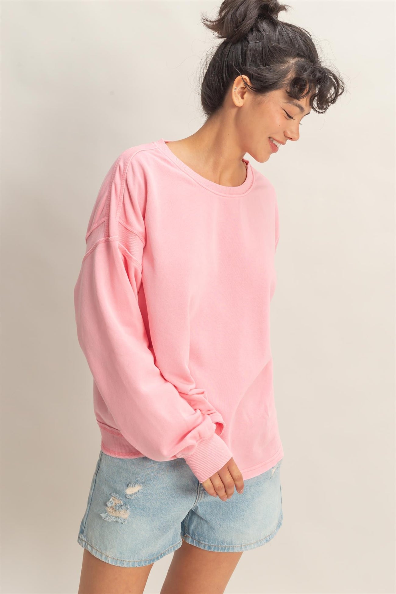 woman wearing a pink oversized sweatshirt with long sleeves and denim shorts