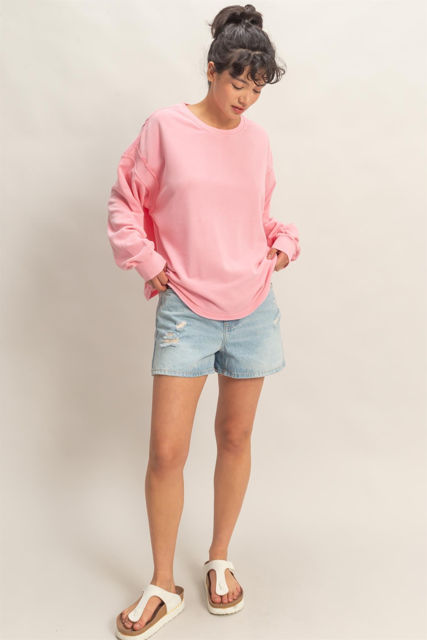 woman wearing a oversized pink sweatshirt and distressed denim shorts, standing with hands in pockets