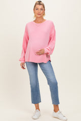 woman wearing a pink oversized maternity top and blue cropped jeans, holding her baby bump