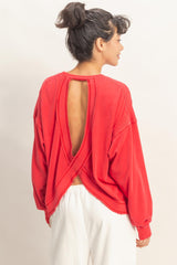 woman wearing a red oversized sweatshirt with an open back and long sleeves, styled casually with white pants