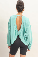 woman wearing a turquoise oversized sweatshirt with an open back and long sleeves, paired with black shorts