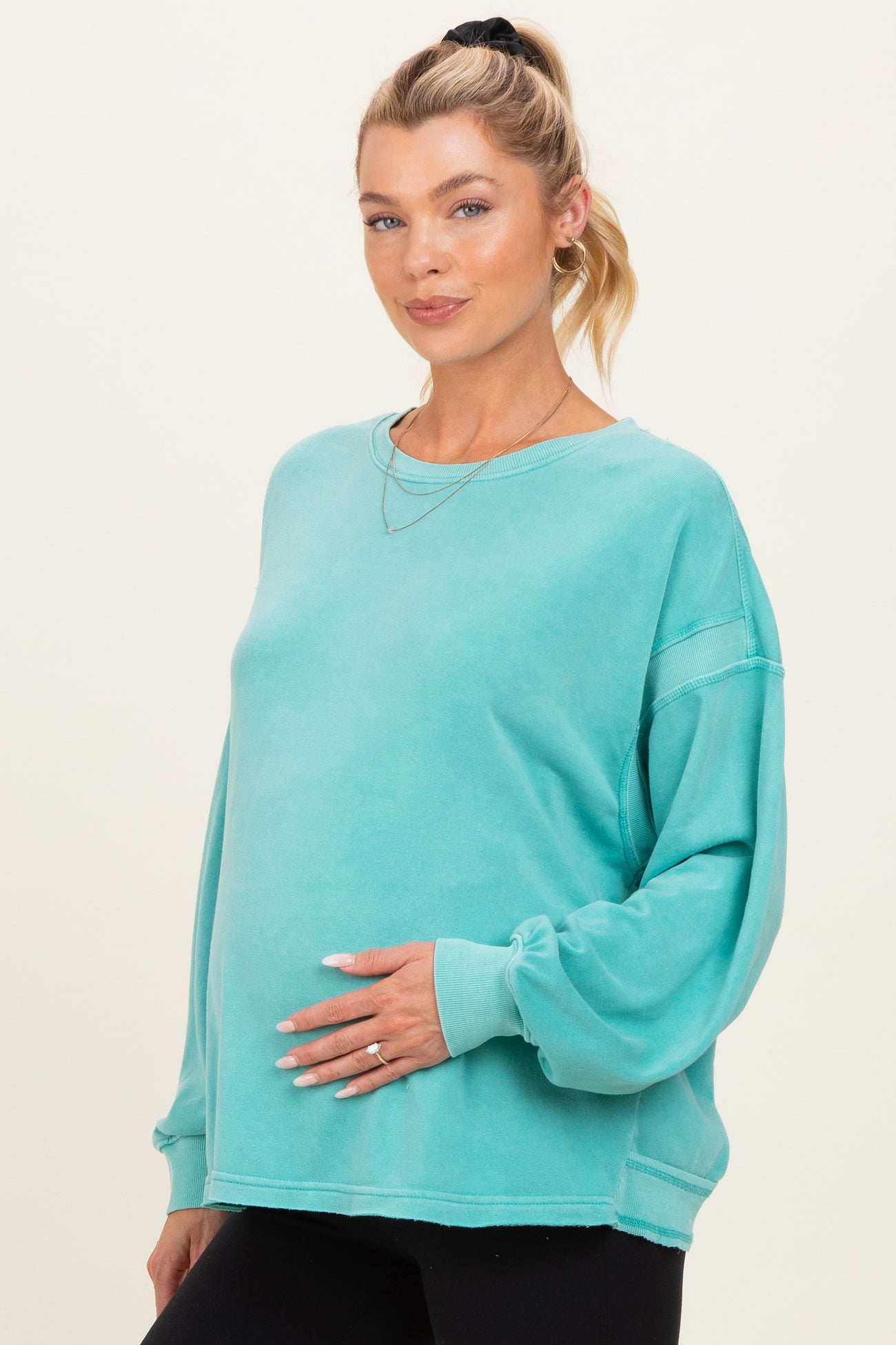 woman wearing a teal oversized maternity sweatshirt with long sleeves and a visible baby bump