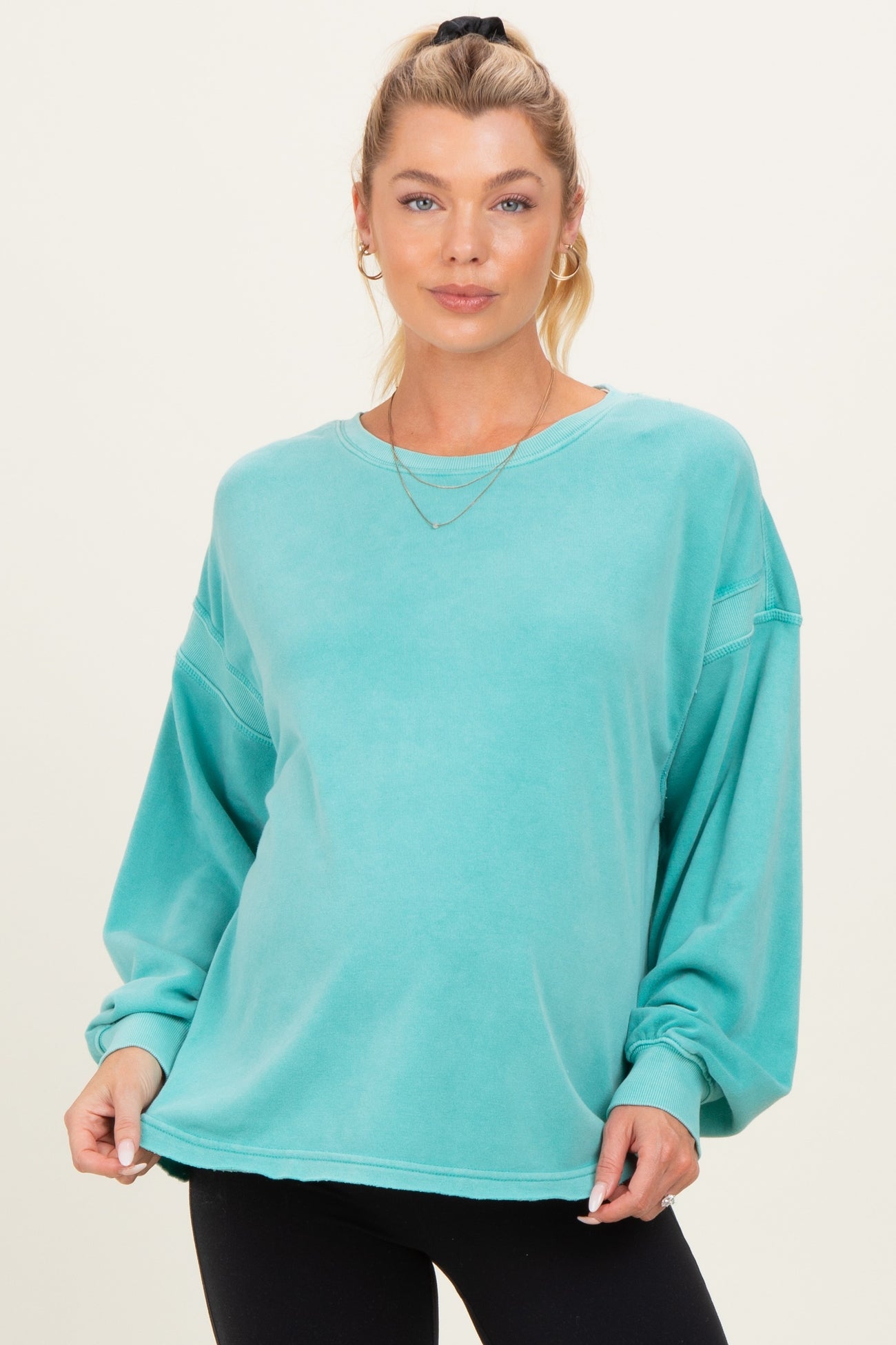 woman wearing a teal oversized sweatshirt with long sleeves and a relaxed fit, showing her baby bump