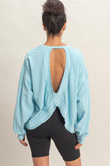 woman wearing a light blue oversized sweater with an open back detail paired with black bike shorts