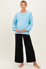 woman wearing a light blue oversized maternity top and black wide-leg pants, holding her baby bump