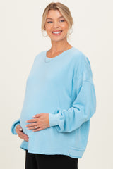 woman wearing a light blue oversized maternity sweatshirt and highlighting her baby bump