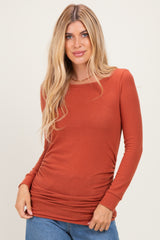 woman wearing a rust long sleeve fitted top with ruching details, styled with blue denim jeans