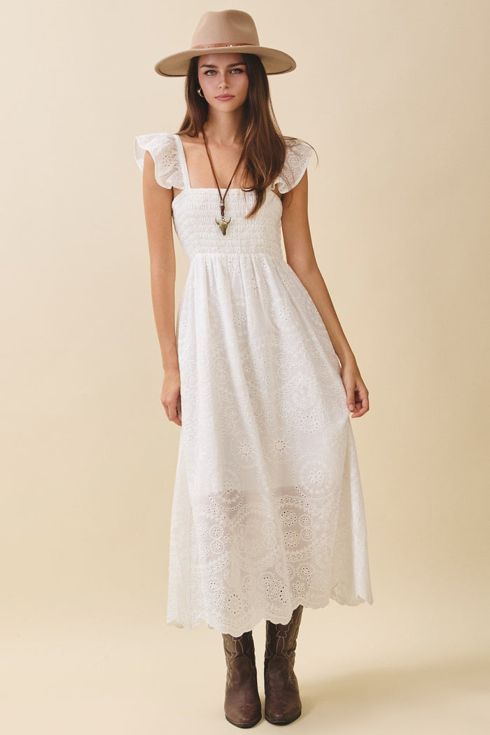 woman wearing a white maxi dress with ruffle sleeves and embroidered details, paired with a wide-brimmed hat and brown boots
