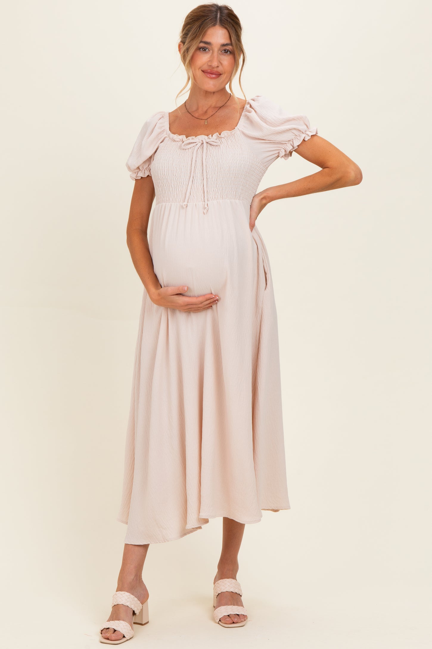 woman wearing a light pink maternity dress with puff sleeves and a smocked bodice, holding her baby bump