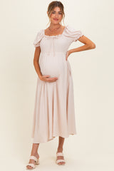 woman wearing a light pink maternity dress with puff sleeves and a smocked bodice, holding her baby bump