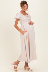 woman wearing a light pink maternity maxi dress with short puff sleeves and pockets, cradling her baby bump