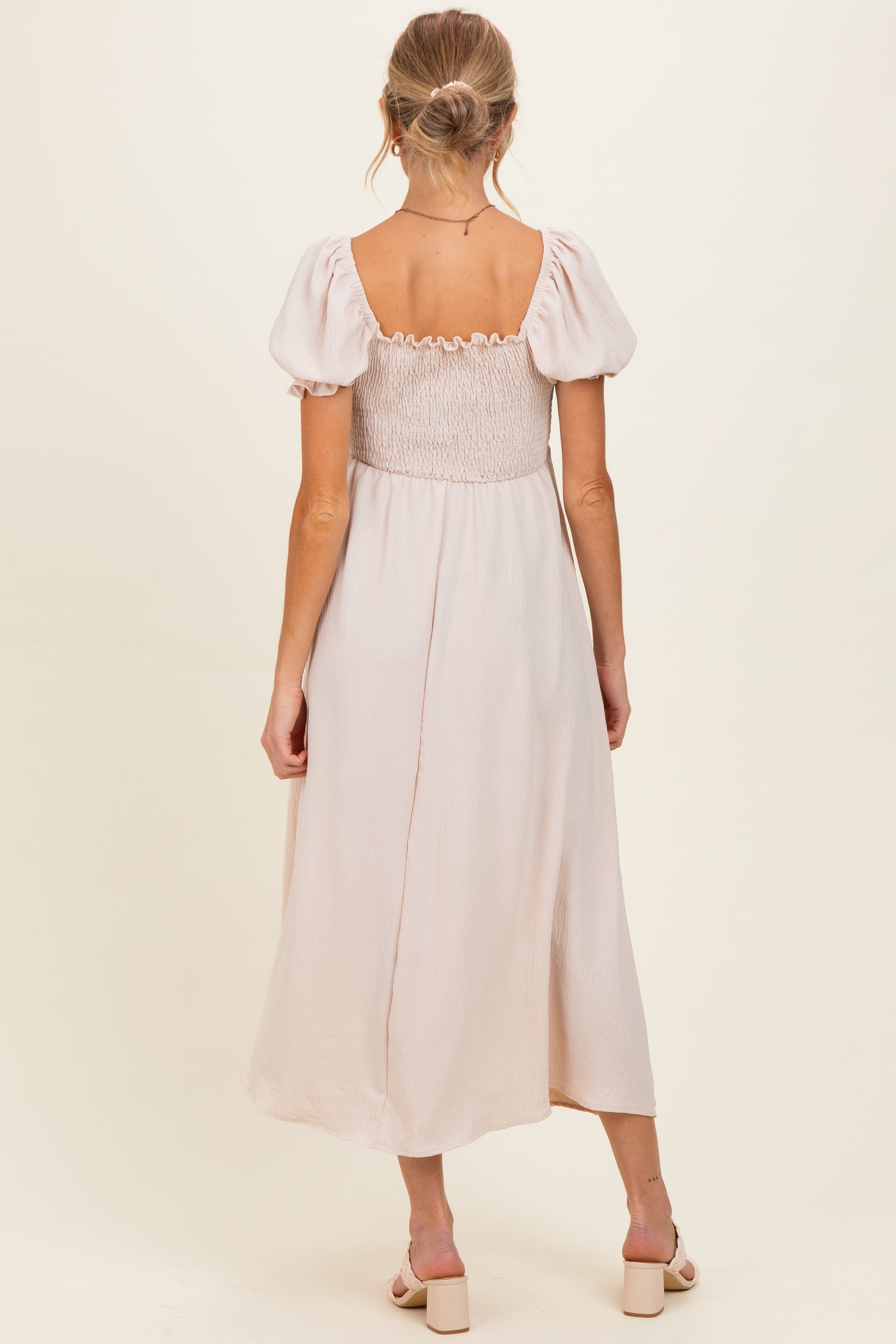 woman wearing a light pink maternity dress with puff sleeves and a smocked bodice, viewed from the back