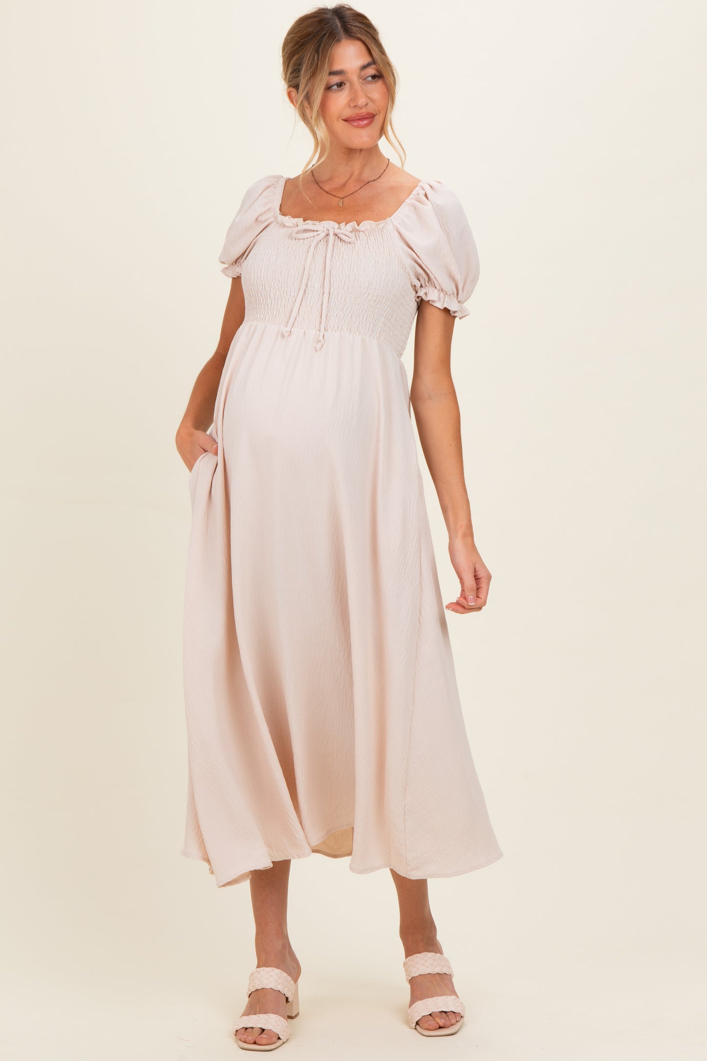 woman wearing a light pink maternity dress with puff sleeves and a tie front, showcasing her baby bump