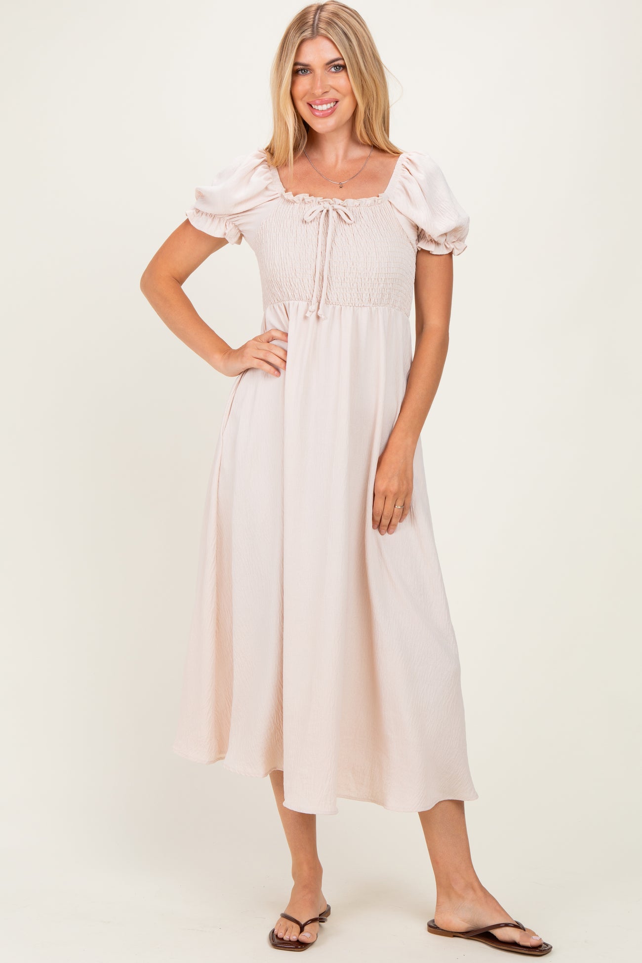woman wearing a light pink puff sleeve midi dress with a smocked bodice and a tie detail at the neckline
