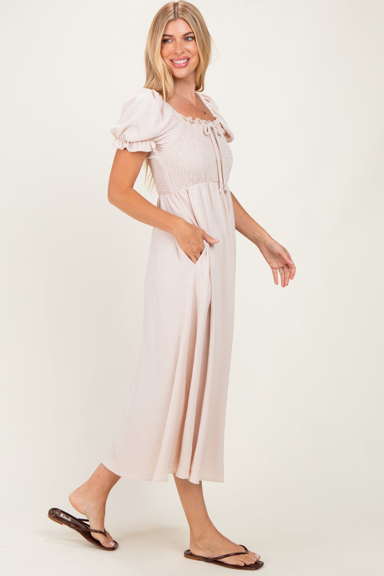 woman wearing a light pink midi dress with short puff sleeves and pockets, standing in profile