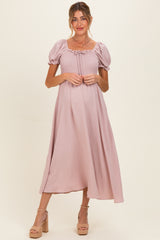 woman wearing a light pink maternity maxi dress with puff sleeves and a smocked bodice, holding her baby bump