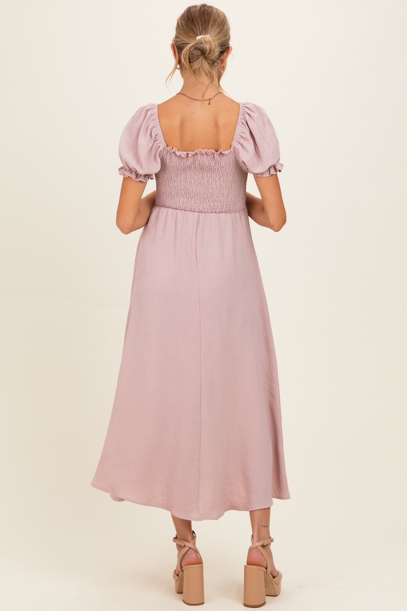 woman wearing a light pink maternity dress with puff sleeves and a smocked bodice, showing the back view