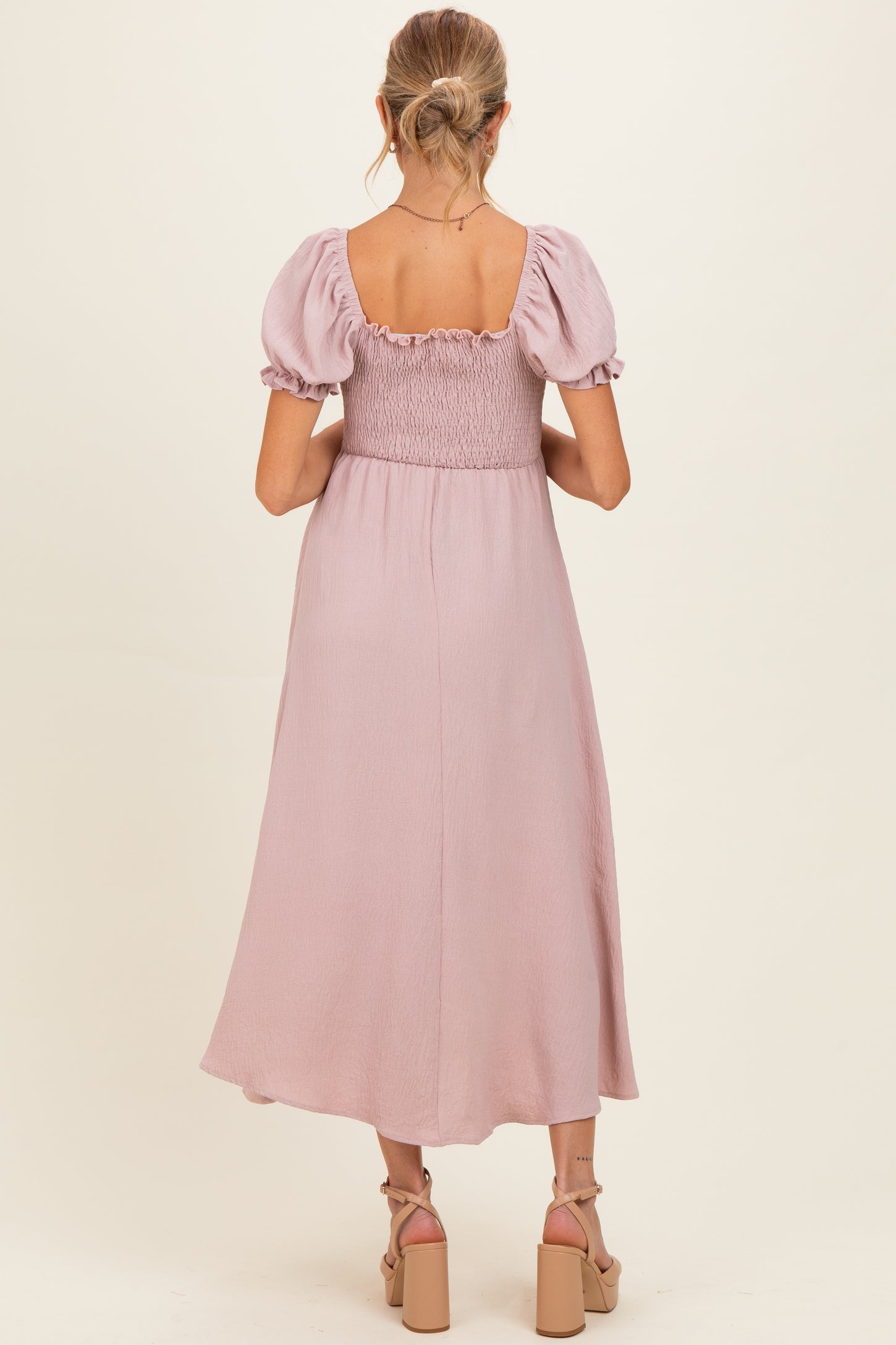 woman wearing a light pink maternity dress with puff sleeves and a smocked bodice, showing the back view