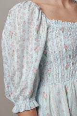 woman wearing a light blue floral smocked dress with puff sleeves and a square neckline