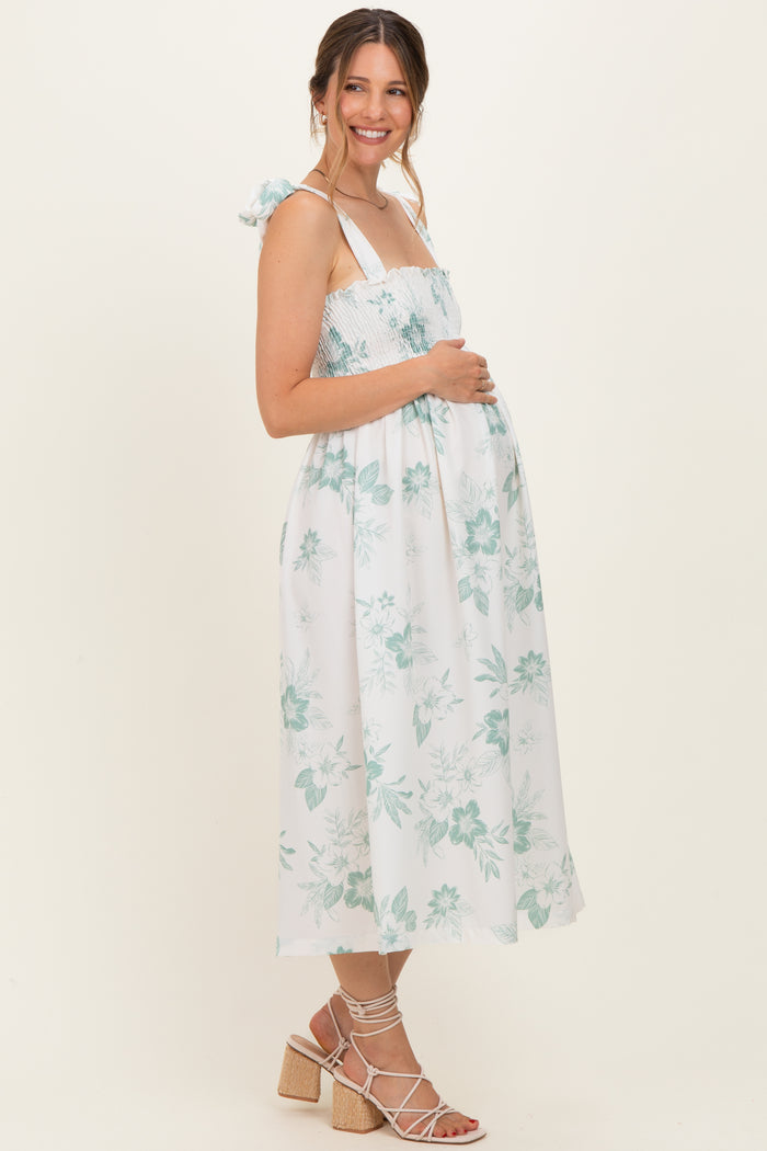 woman wearing a white floral maternity dress with adjustable straps and a visible baby bump