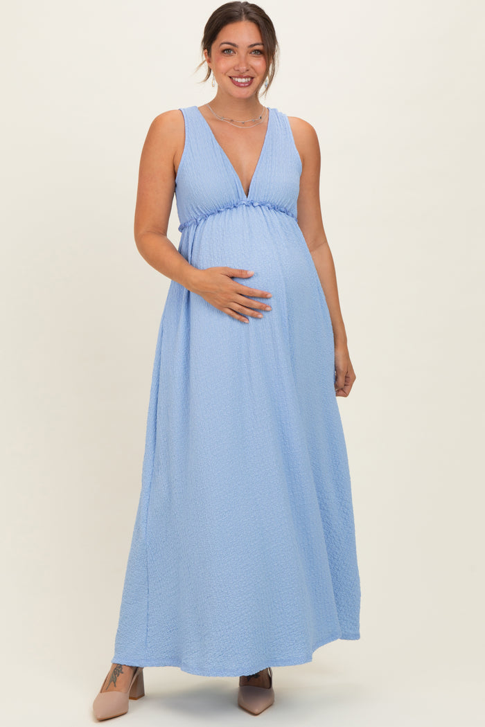 woman wearing a light blue sleeveless maxi maternity dress with a plunging neckline and holding her baby bump