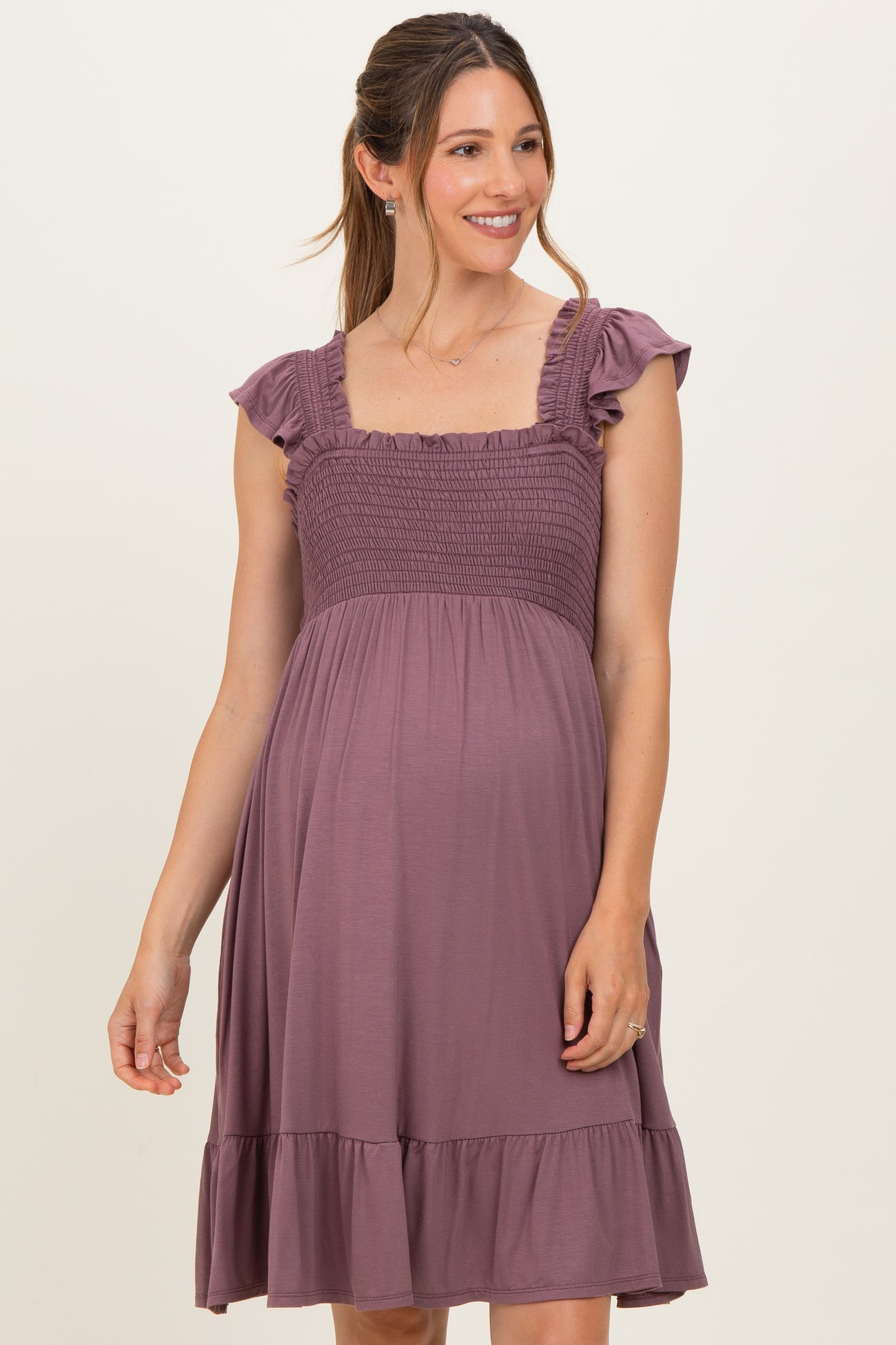 woman wearing a lavender maternity dress with ruffled sleeves and a smocked bodice, showcasing her baby bump