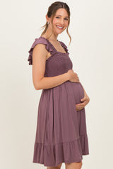 woman wearing a mauve maternity dress with ruffled straps and a flowing skirt, gently cradling her baby bump