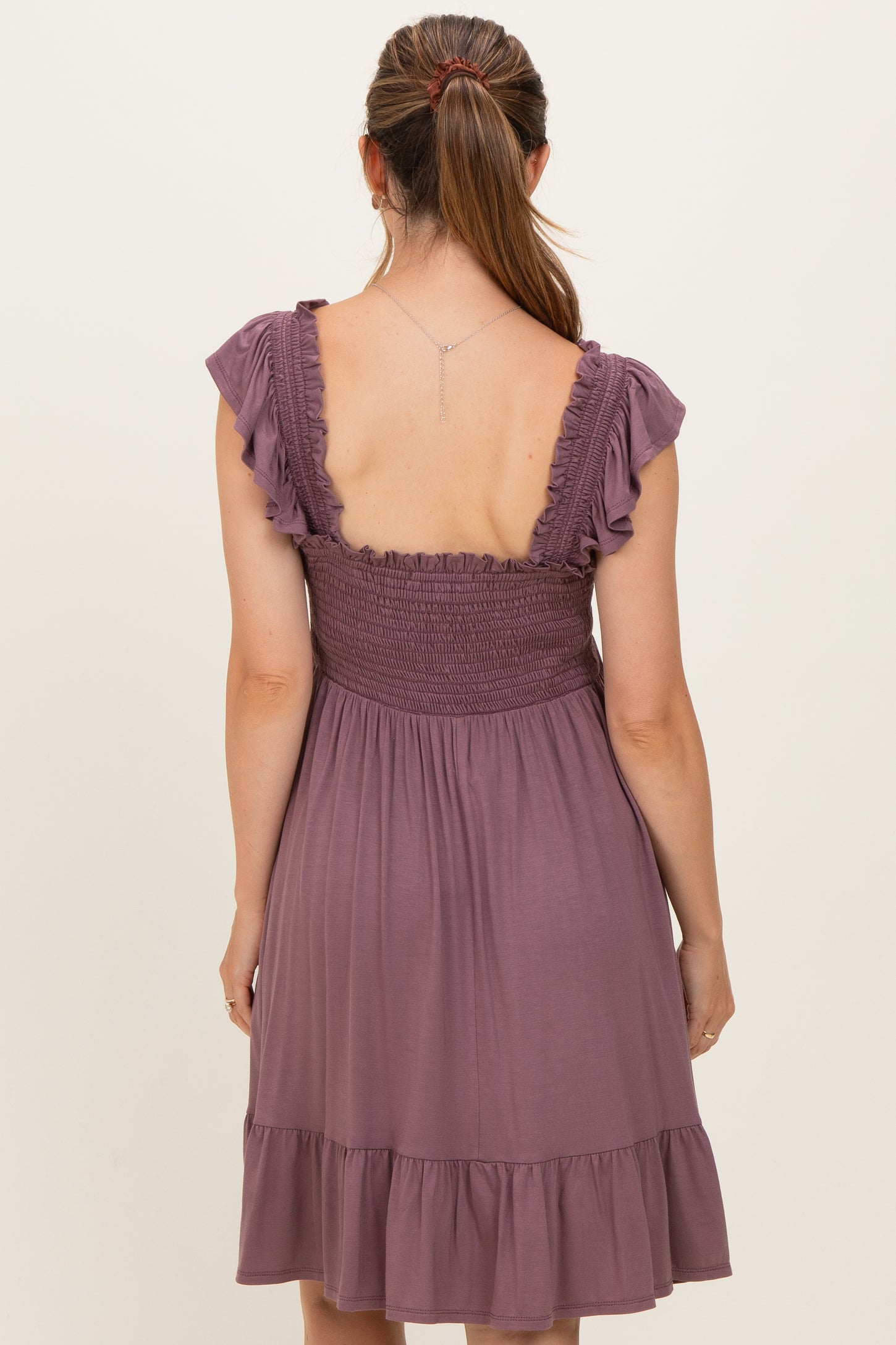 woman wearing a lavender maternity dress with a smocked bodice and ruffled sleeves, showing the back view