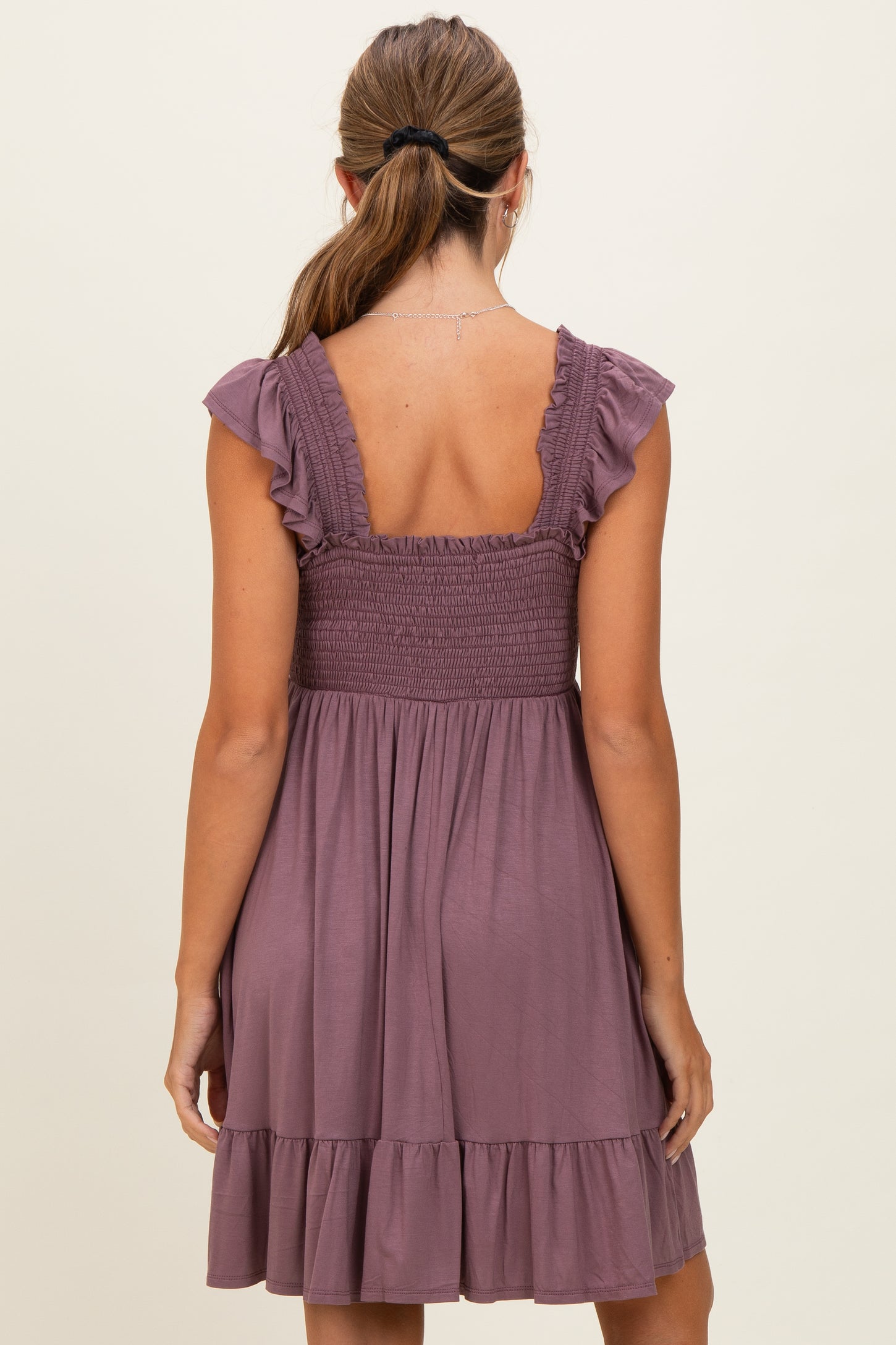 woman wearing a mauve sleeveless dress with ruffled straps and a shirred bodice, featuring a tiered skirt at the hem