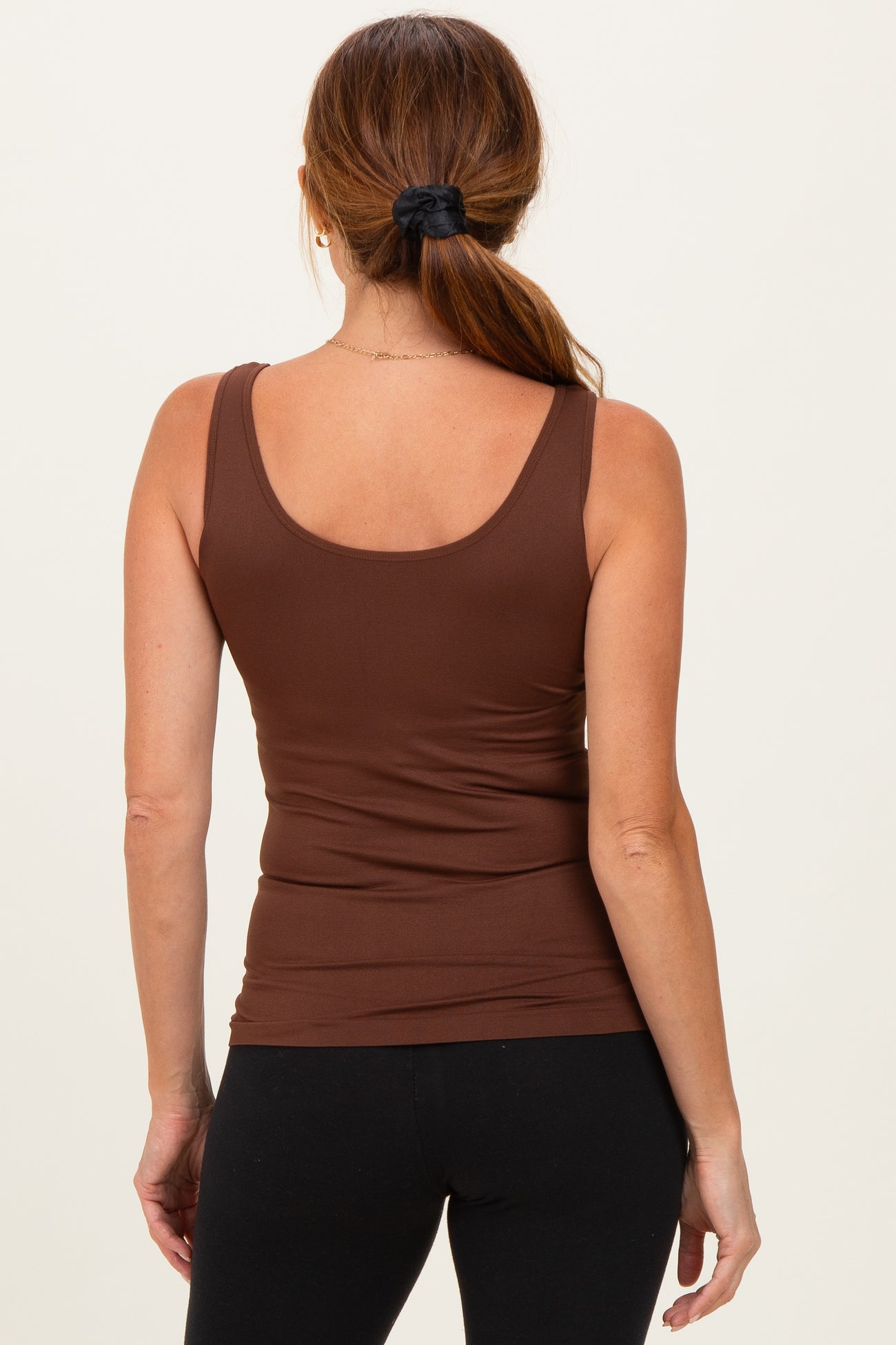 woman wearing a brown sleeveless fitted tank top with a scoop neckline and black leggings, seen from the back