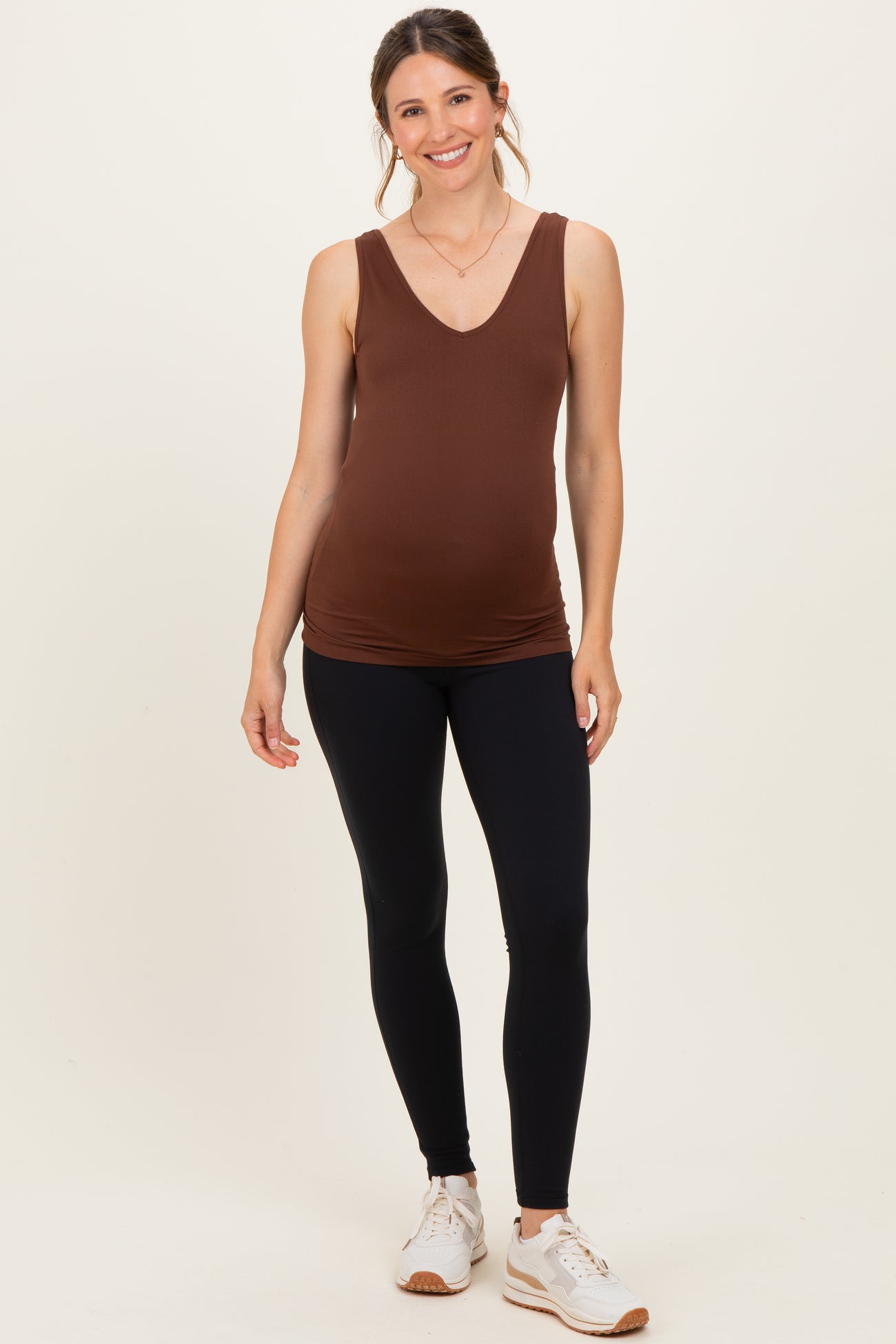 woman wearing a brown v-neck maternity tank top with black leggings and sneakers, showing a visible baby bump