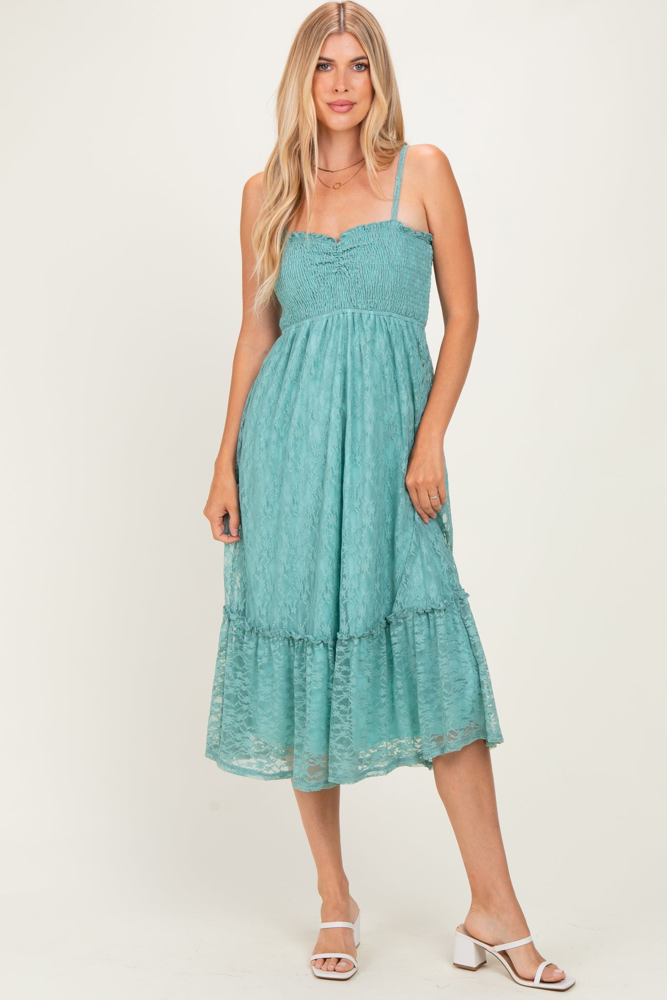woman wearing a teal smocked midi dress with lace detailing and a ruffled hem, paired with white block heel sandals