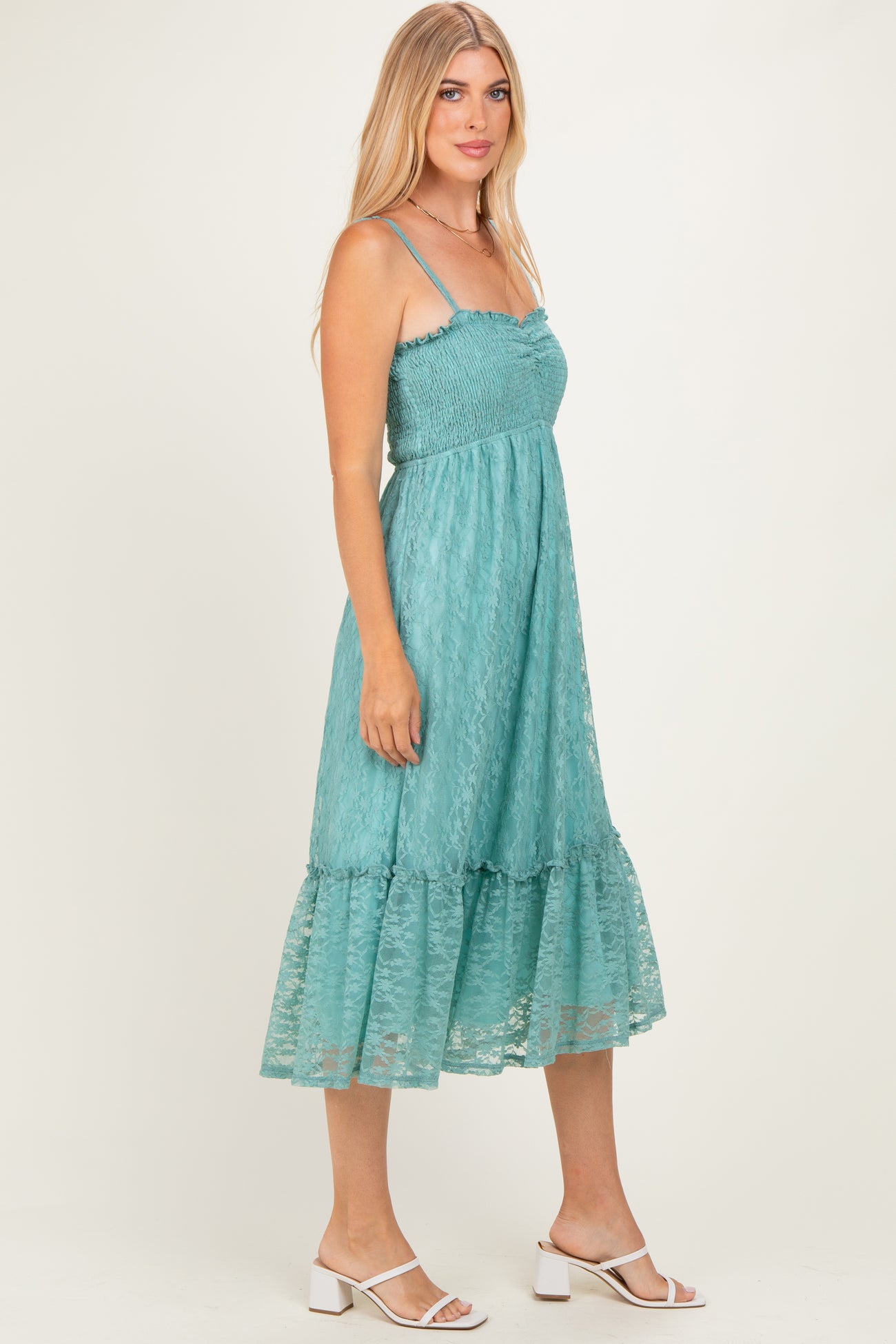 woman wearing a teal lace midi dress with spaghetti straps and a ruffled hem, standing in profile