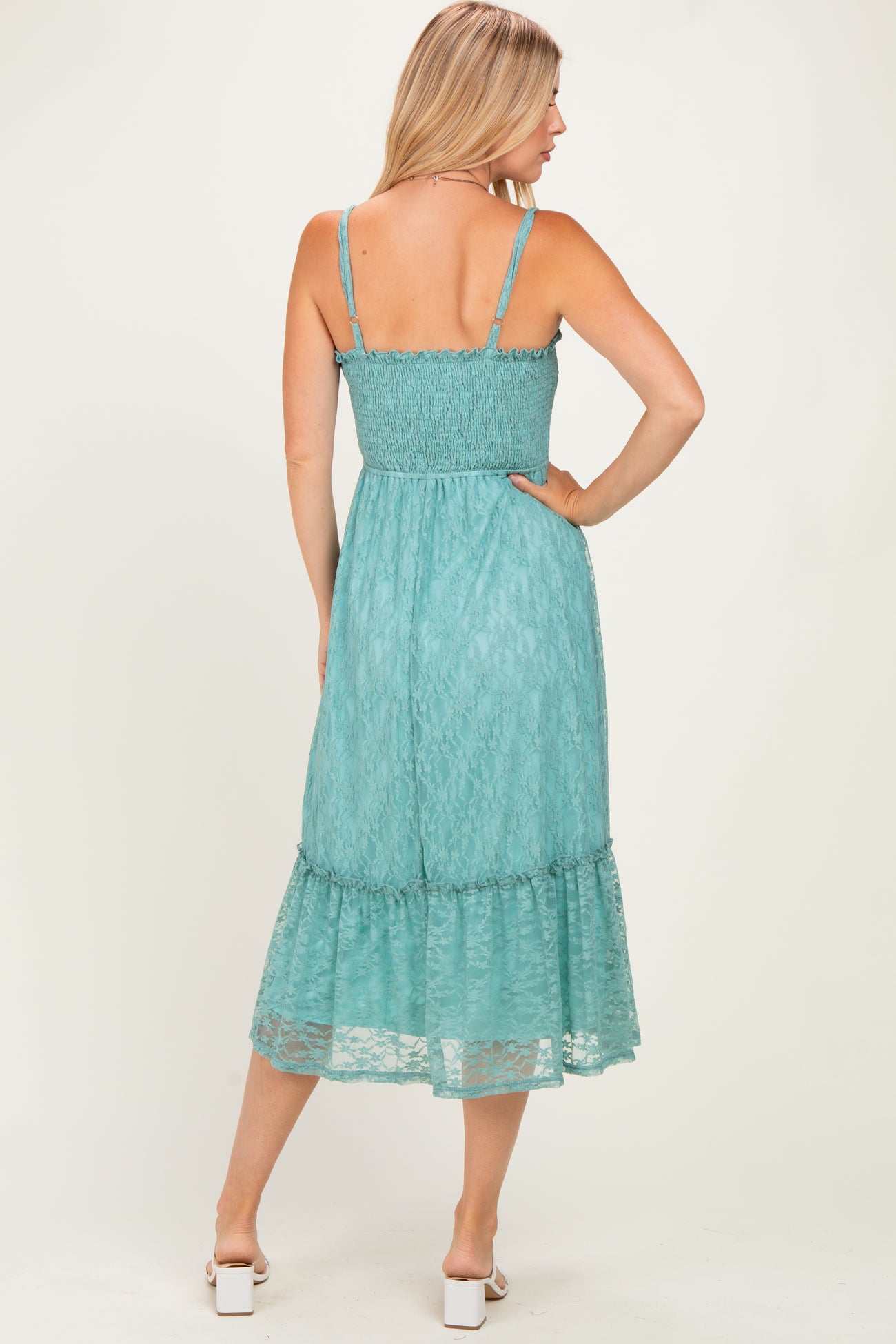 woman wearing a back view of a light teal spaghetti strap dress with a smocked bodice and ruffled hem