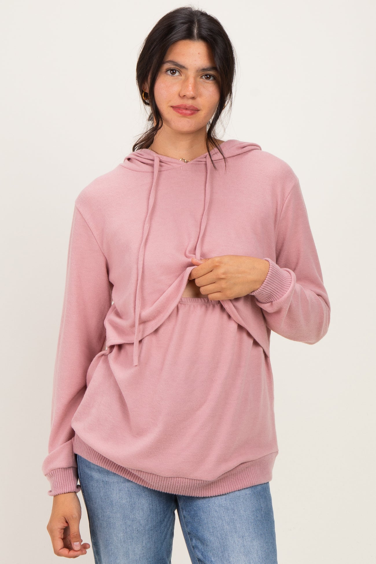 woman wearing a light pink hooded sweatshirt with a adjustable front panel and loose fit, paired with blue jeans