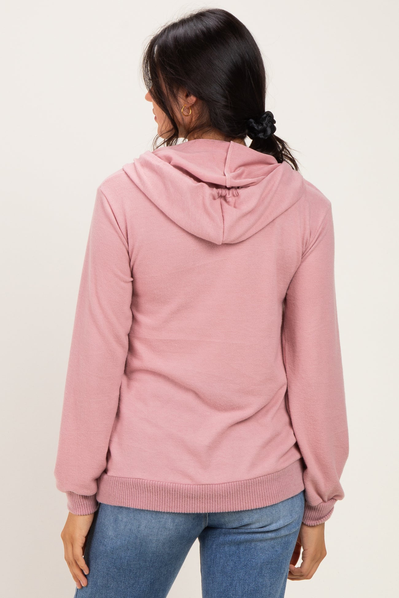 woman wearing a pink hoodie with a front pocket and drawstring hood, paired with blue jeans