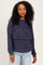 woman wearing a navy blue hooded sweatshirt with a layered look and long sleeves, standing with a slight smile