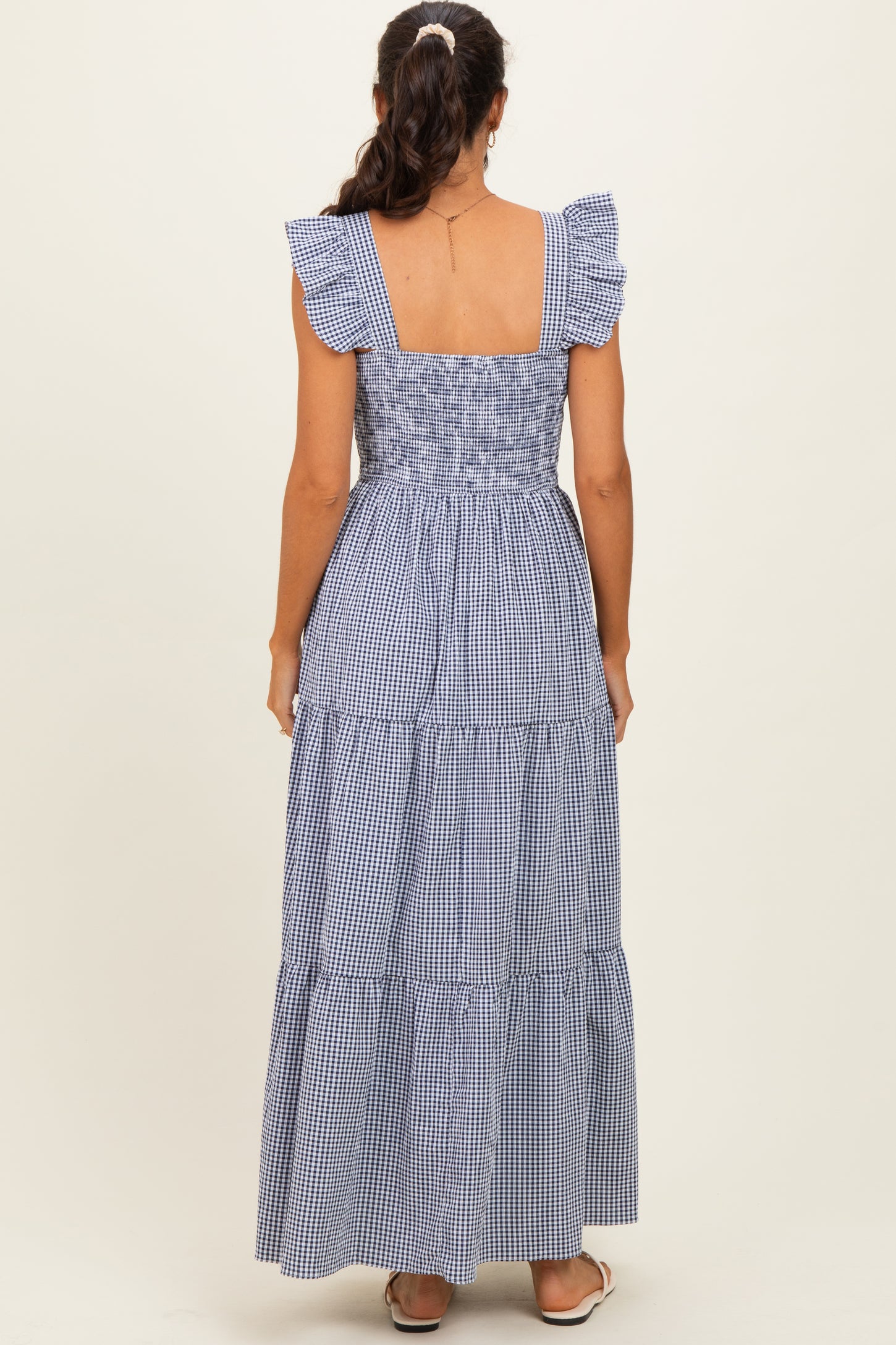 woman wearing a navy and white gingham maxi dress with ruffled sleeves and tiered skirt, seen from the back