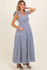 woman wearing a blue and white gingham maternity maxi dress with ruffled straps and pockets, showing her baby bump
