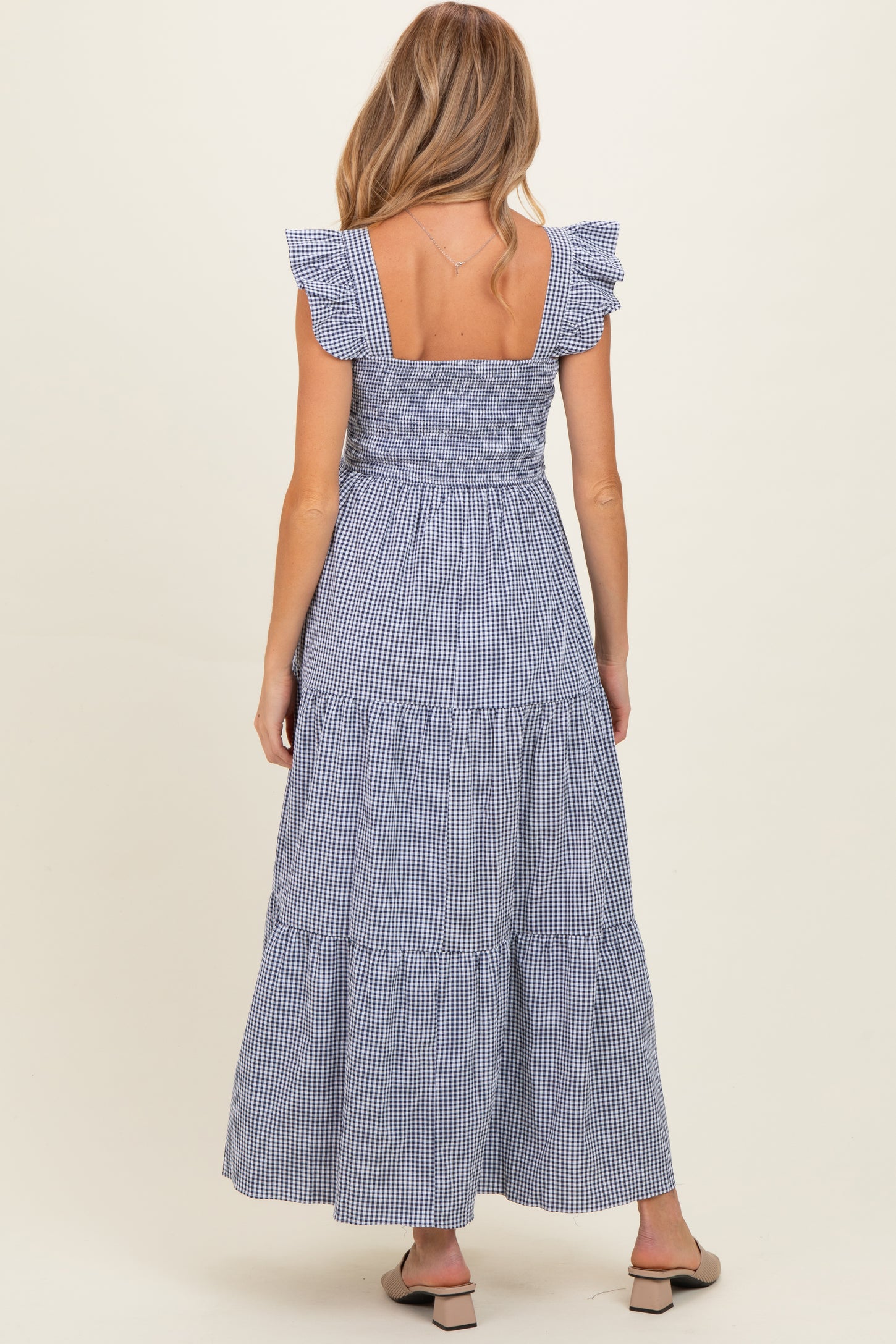woman wearing a navy and white gingham maternity maxi dress with ruffled sleeves and a tiered skirt, seen from the back