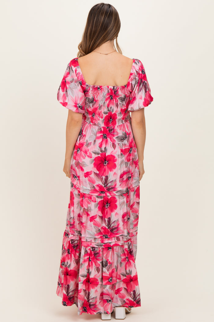 woman wearing a pink floral maternity maxi dress with puff sleeves and a tiered design, showing off her baby bump from behind