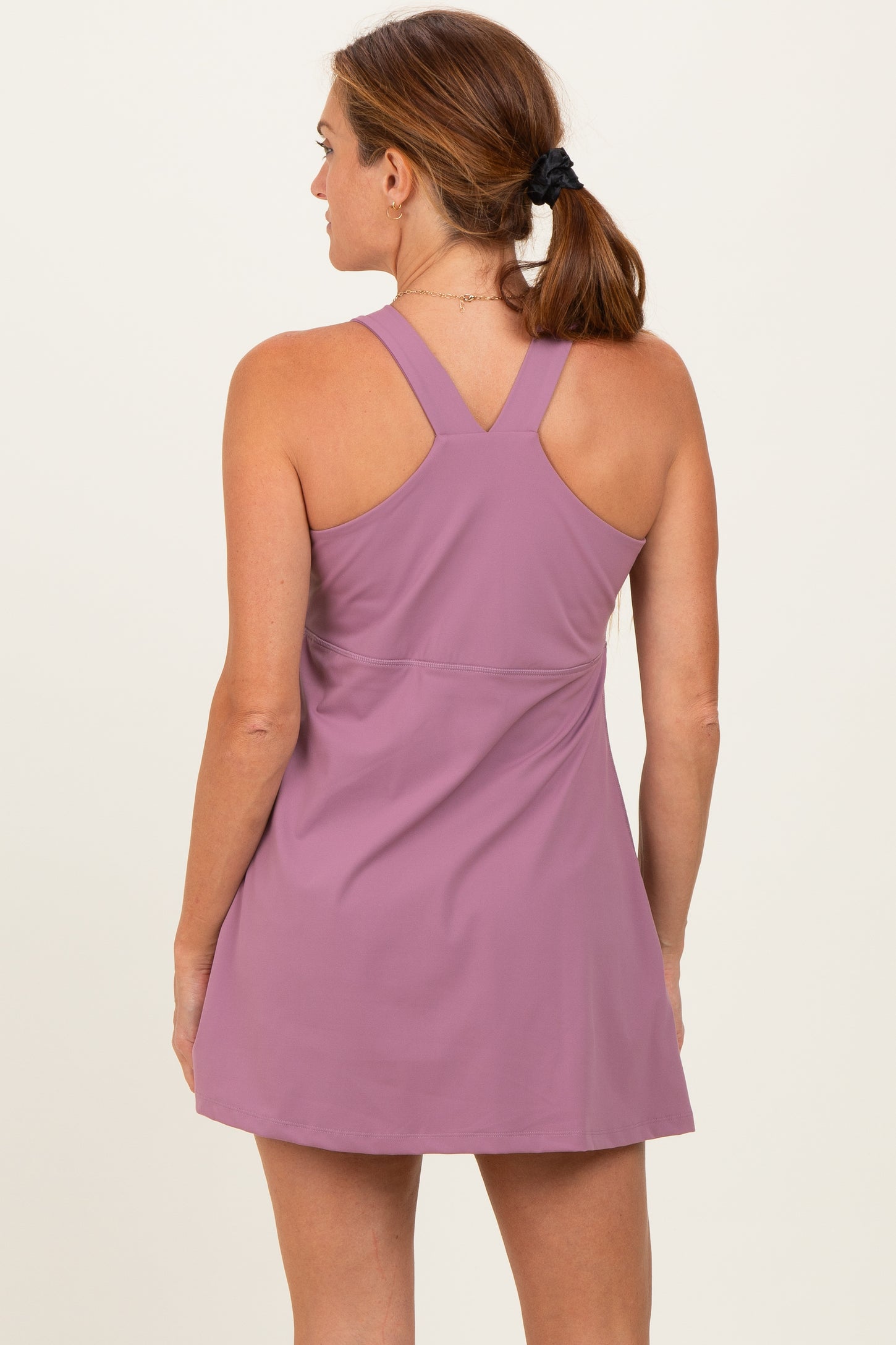 woman wearing a mauve sleeveless tennis dress with a fitted bodice and flared skirt viewed from the back
