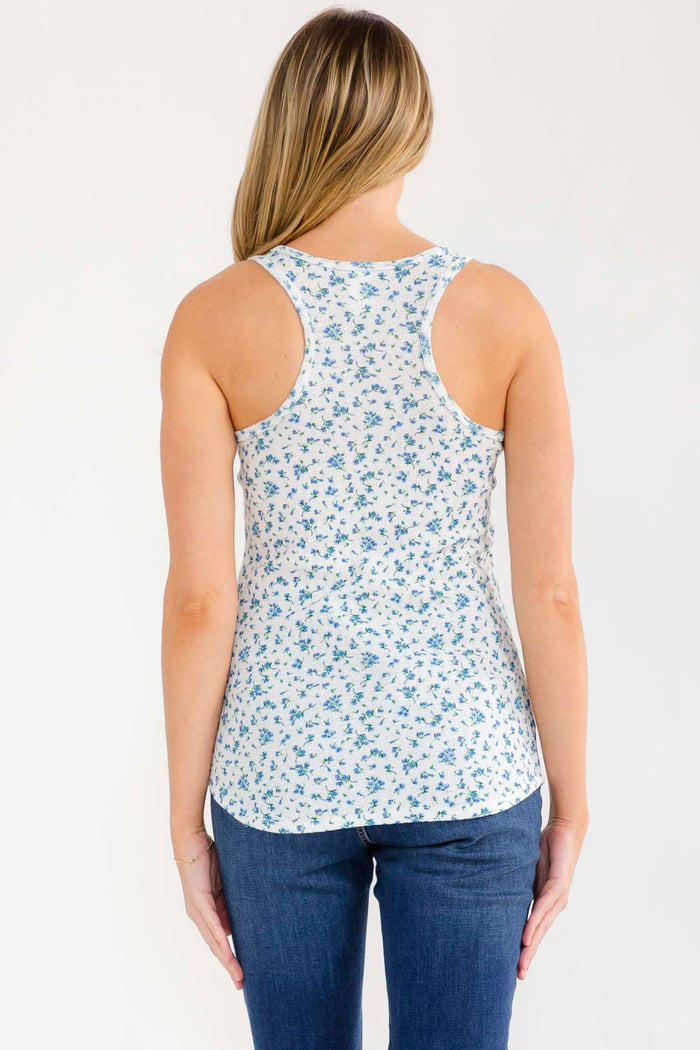 woman wearing a white tank top with small blue floral prints and blue jeans, viewed from the back