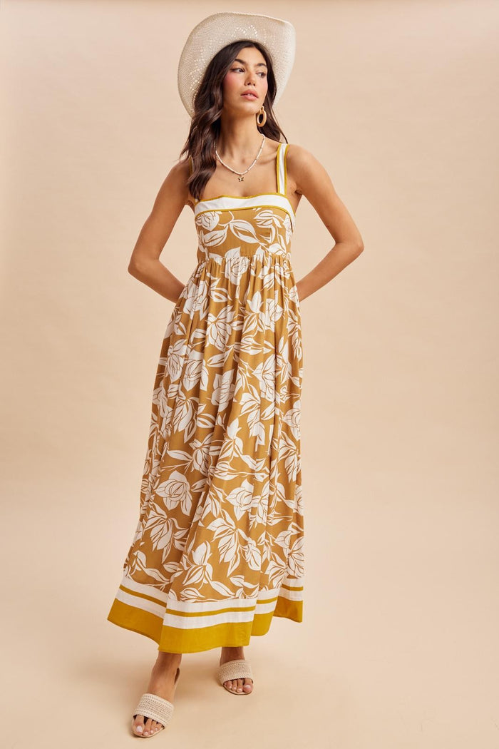 woman wearing a mustard yellow floral maxi dress with thin straps and a flared hem, styled with a wide-brimmed hat