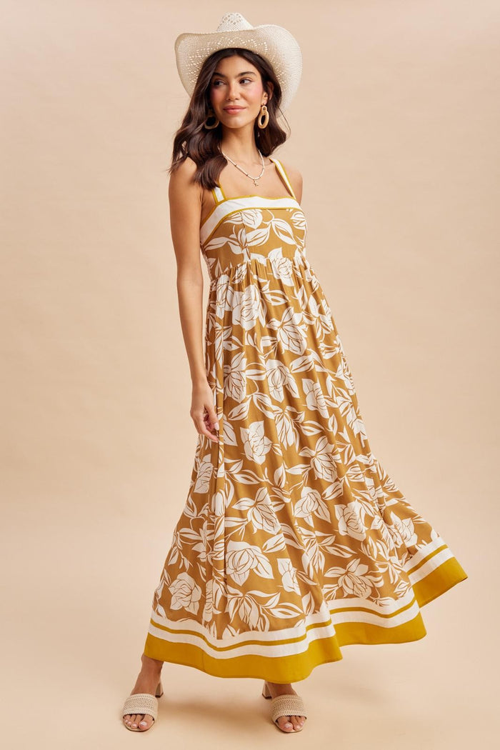 woman wearing a mustard yellow floral maxi dress with a fitted bodice and flowy skirt, styled with a white cowboy hat