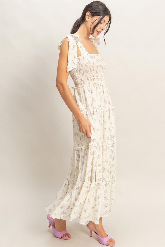 woman wearing a cream floral maxi dress with ruffled tiers and bow-tie straps, styled with purple heels