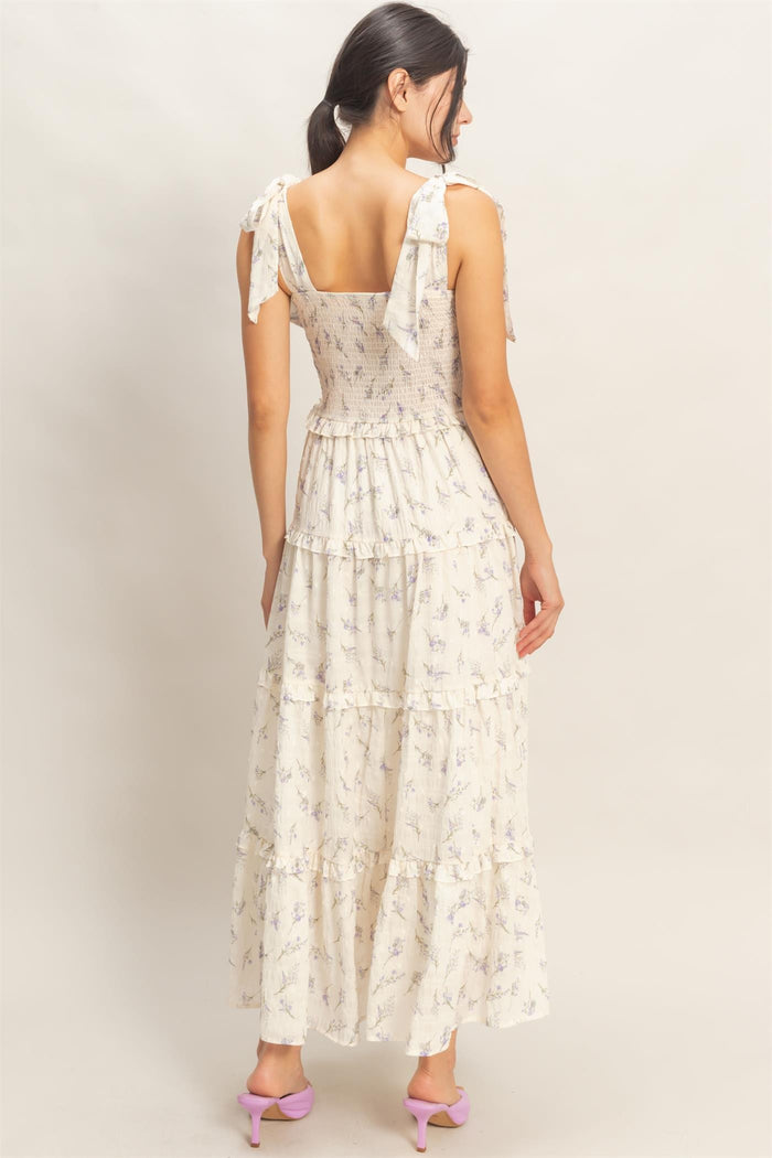 woman wearing a floral print maxi dress with tied shoulder straps and a tiered skirt, shown from the back