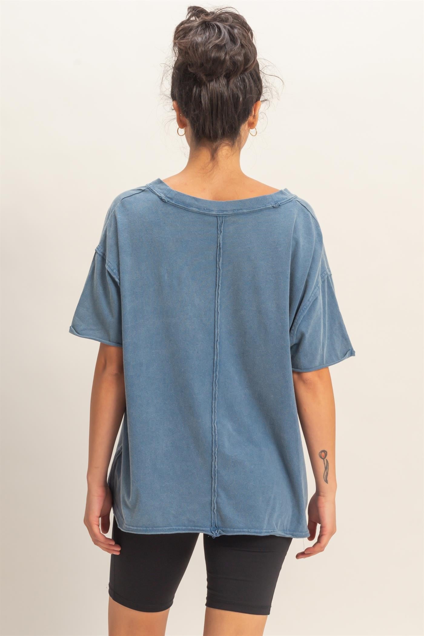 woman wearing a loose-fit blue oversized t-shirt with a raw hem and back seam, paired with black shorts.