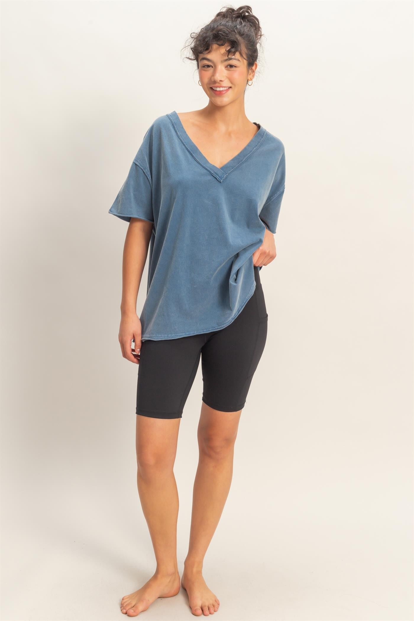 woman wearing a blue oversized v-neck t-shirt with black biker shorts and standing barefoot